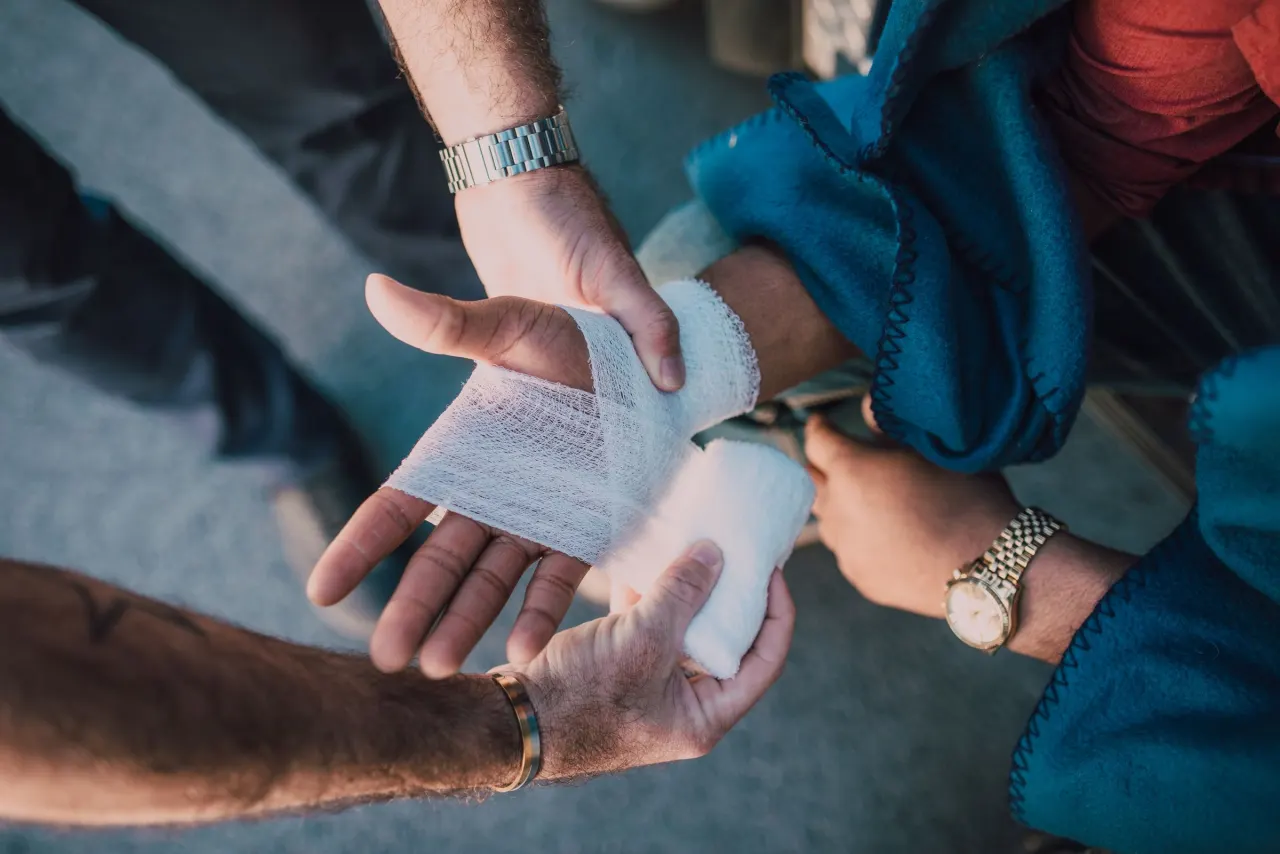Hands applying a clean dressing to a wound on a forearm during basic first aid