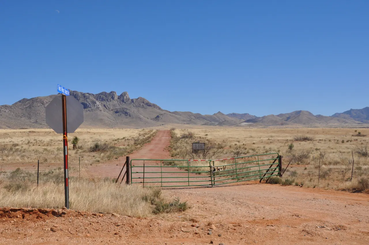 A closed wire ranch gate across a dirt road near Valentine, Texas, with dry scrub and distant mountains under a clear sky